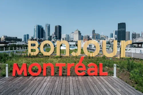 City Of Montreal day time skyline. The words Tourisme/ Montréal/Montre’al written over it. The word bonjour appears made of pine in foreground