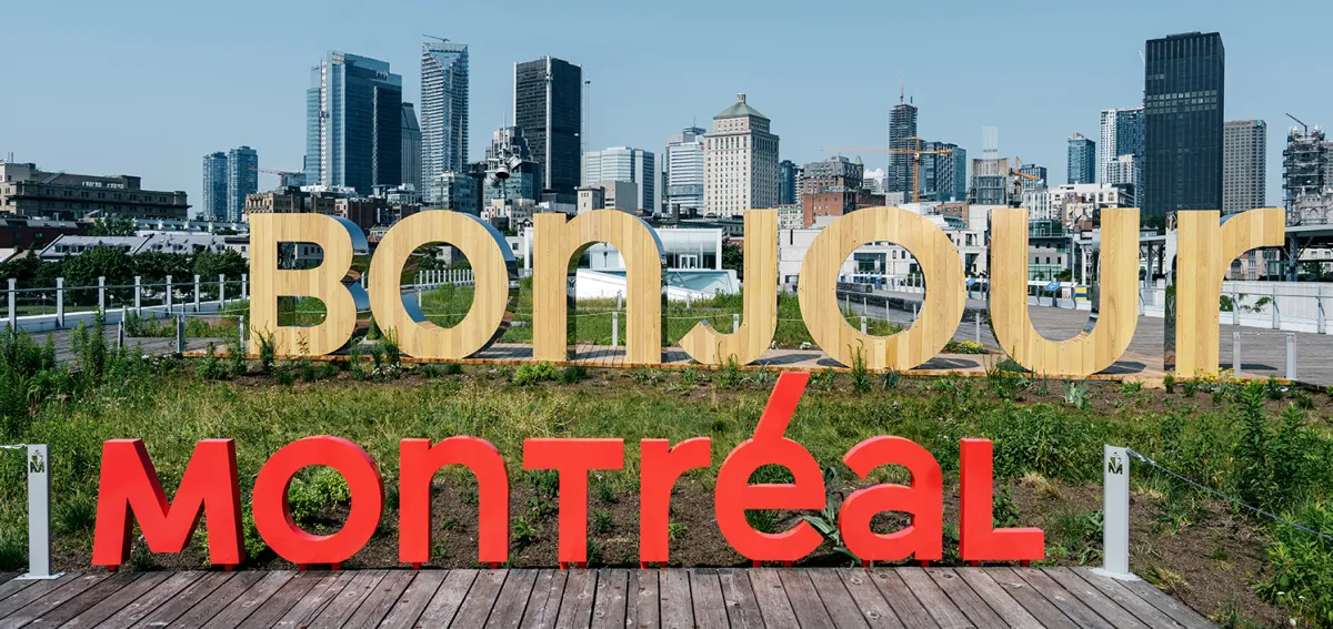 City Of Montreal day time skyline. The words Tourisme/ Montréal/Montre’al written over it. The word bonjour appears made of pine in foreground